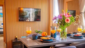 A dining area with a table set for breakfast, a television mounted on the wall, and a window with curtains. - 4.97 Super Host`s New Boutique & Prime Location (Limassol)