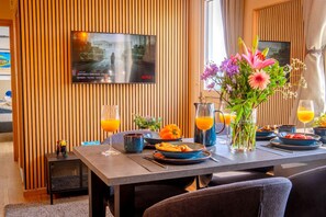 A dining area with a table set for breakfast, a television mounted on the wall, and a window with curtains. - 4.97 Super Host`s New Boutique & Prime Location (Limassol)