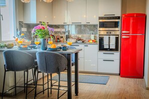 Une cuisine moderne avec un coin repas, comprenant un réfrigérateur rouge, des appareils en acier inoxydable et un vase avec des fleurs sur la table.
