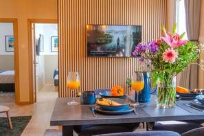 Une chambre d’hôtel avec une table à manger dressée pour le petit-déjeuner, un téléviseur fixé au mur et une vue sur l’extérieur.
