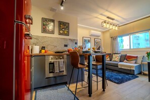 A modern kitchen with a built-in oven, a dining area with two chairs, and a sofa with colorful cushions. - 4.97 Super Host`s New Boutique & Prime Location (Limassol)