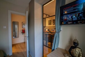 A modern living room with a television displaying a movie, a dining area with a table and chairs, and a kitchen visible through an open door. - 4.97 Super Host`s New Boutique & Prime Location (Limassol)