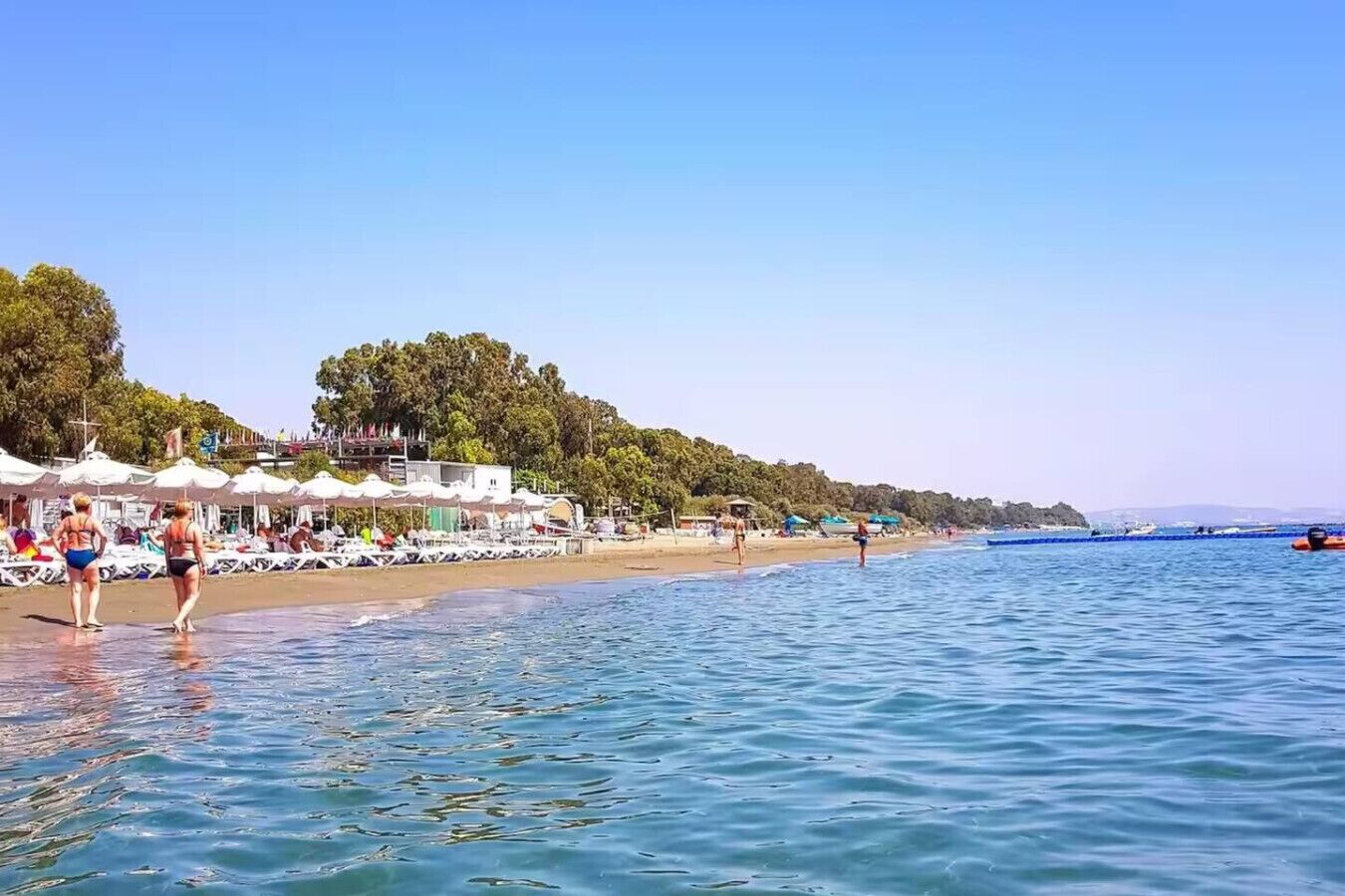 Una playa con sombrillas, gente y barcos.