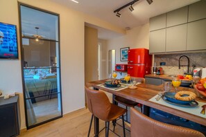 Une cuisine moderne avec un îlot central en bois, des tabourets de bar, un réfrigérateur rouge et une porte vitrée donnant sur un balcon.