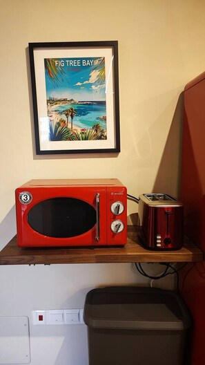 A red microwave on a wooden shelf with a framed picture of a beach scene above it. - 4.97 Super Host`s New Boutique & Prime Location (Limassol)