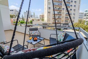 A balcony with a swing chair, a table with fruit and a glass of orange juice, and a view of residential buildings. - 4.97 Super Host`s New Boutique & Prime Location (Limassol)