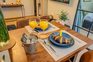 Een eettafel met een maaltijd, twee glaasjes jus d'orange, een warme drank en een decoratieve Boeddha-beeldje.