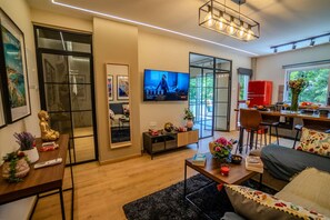 A modern living room with a flat-screen TV, a dining area with a red chair, and a kitchen visible through an open door. - 4.97 Super Host`s New Boutique & Prime Location (Limassol)