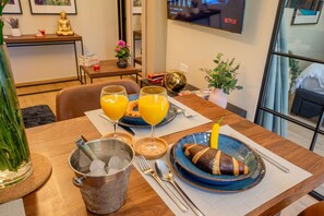 Ein Esstisch mit einem warmen Getränk, zwei Orangensaftgläsern, einem Teller mit einem Croissant und einer Schüssel mit Eiswürfeln.