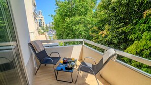 Un balcone con due sedie, un tavolino e vista su piante e edifici.