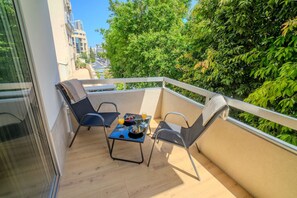 Ein Balkon mit zwei Stühlen, einem kleinen Tisch und Blick auf Grünflächen und Gebäude.