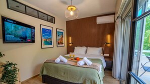Una camera d'albergo con un letto, una televisione, quadri appesi, una pianta e una finestra.