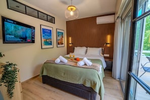 Ein Hotelzimmer mit einem Bett, einem Fernseher, gerahmten Bildern, einer Pflanze und einem Fenster.
