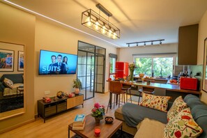 Ein modernes Wohnzimmer mit Fernseher, Sofa, Couchtisch und einem Essbereich mit Küche im Hintergrund.