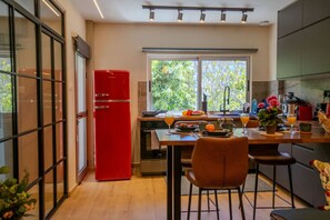 Eine moderne Küche mit einem roten Kühlschrank, einem Esstisch mit Stühlen und einem Fenster mit Blick auf Grünflächen.