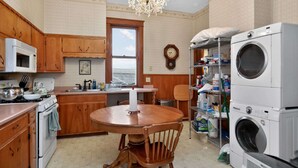 A kitchen with wooden cabinets, a stove, a microwave, a chandelier, a clock, and a stacked washer and dryer.