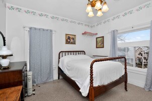 Un dormitorio con una cama de madera, un aparador, un radiador y una ventana con vistas.