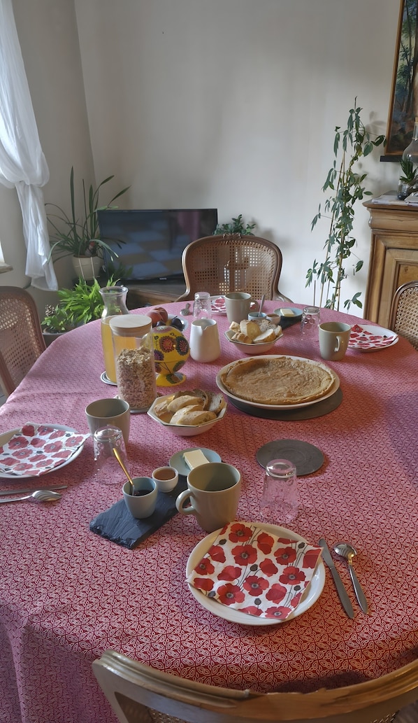 Una mesa de comedor con mantel estampado, varios platos, tazas y un televisor al fondo.