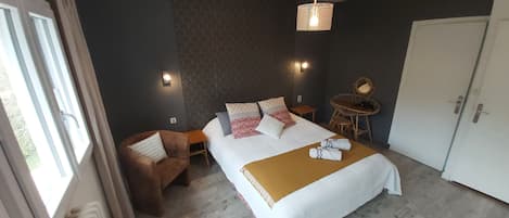 A hotel room with a bed, a chair, a small table, a wardrobe, and a window.