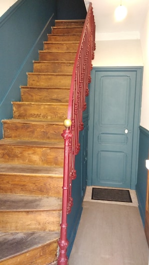 Una escalera de madera con barandilla roja que lleva a una puerta azul.
