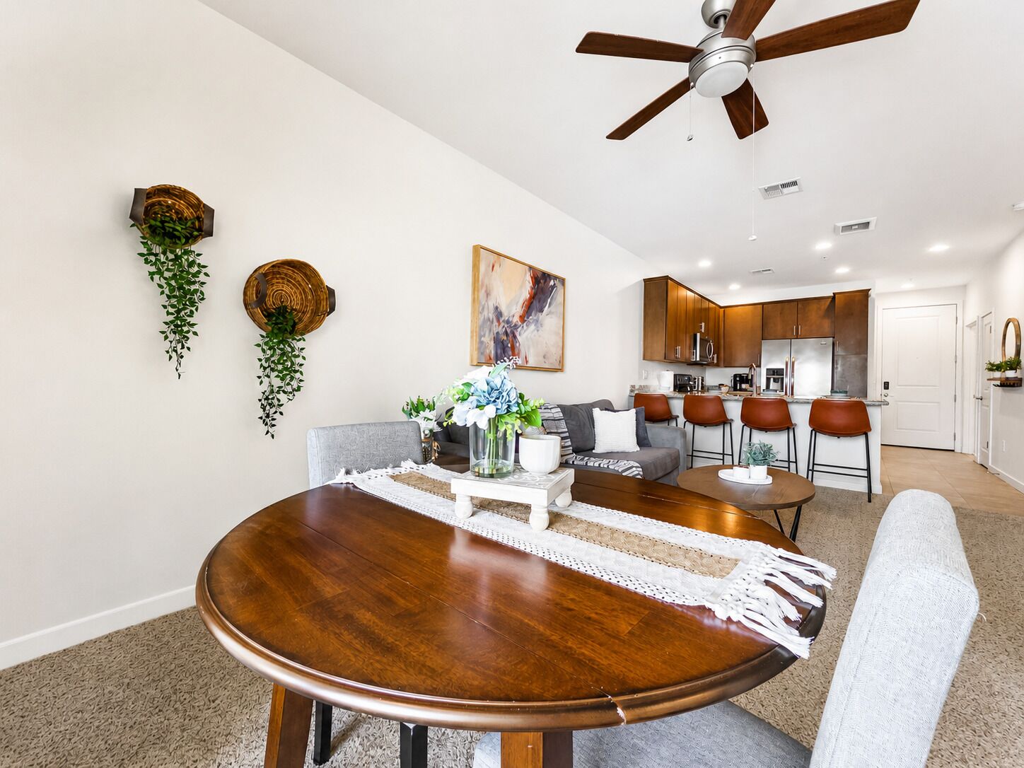 A dining area with a round wooden table, grey upholstered chairs, and a ceiling fan.