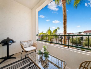 Un balcon avec un fauteuil en osier, une table en verre et un barbecue.