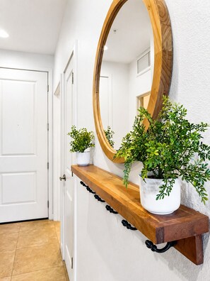 Um corredor com prateleira de madeira contendo plantas em vasos e um espelho grande.