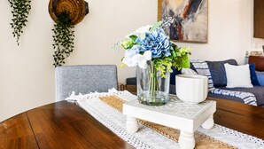 A dining table with a vase of flowers, a white pitcher, and a woven placemat.