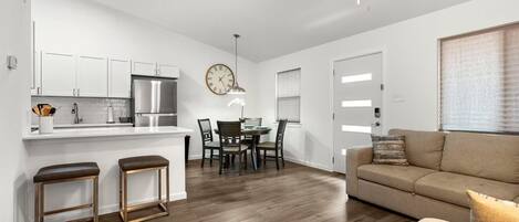 Una cocina moderna con armarios blancos, un refrigerador de acero inoxidable y un comedor con mesa y sillas.