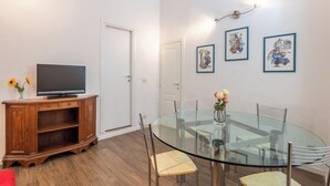 Una sala de estar moderna con una mesa de comedor de vidrio, un televisor de pantalla plana sobre un mueble de madera y dos obras de arte enmarcadas en la pared.