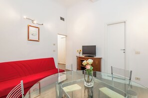 A modern living room with a red sofa, a glass dining table, and a television on a wooden cabinet. - Palazzo Vecchio View by MMega (Firenze)