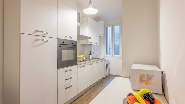 Una cocina moderna con armarios blancos, horno empotrado, lavadora y una ventana que proporciona luz natural.