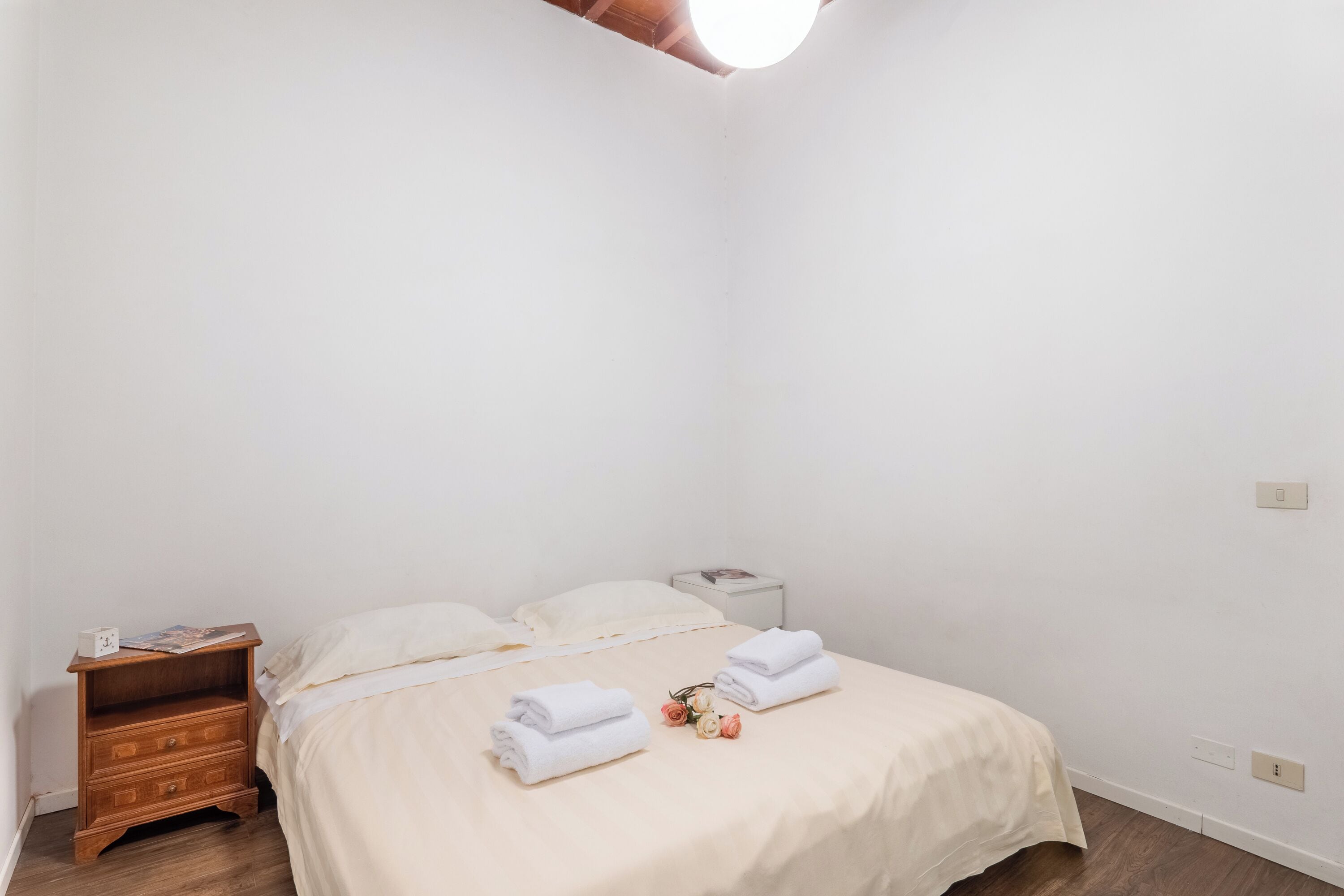 Una habitación sencilla y luminosa con cama, mesita de noche y mesilla.
