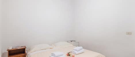 Una habitación sencilla y luminosa con cama, mesita de noche y mesilla.