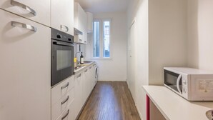Cocina estrecha con horno empotrado, microondas y ventana que deja entrar luz natural.