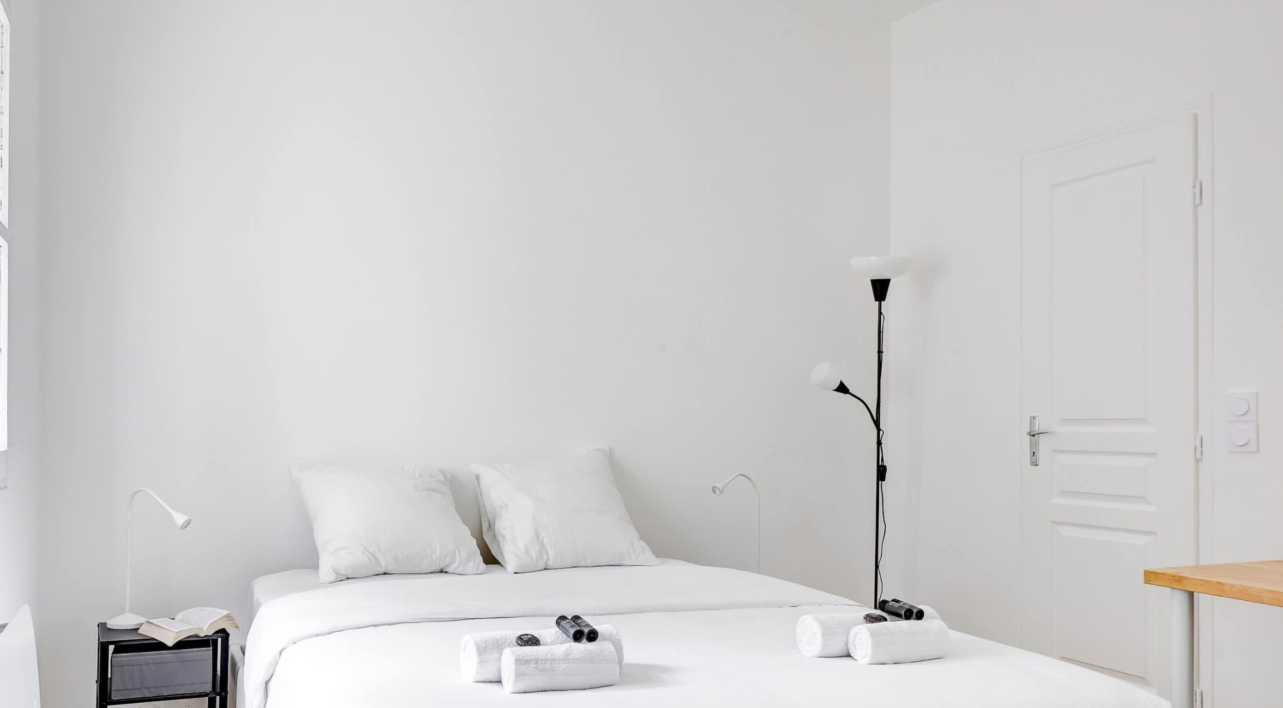 Ein schlicht eingerichtetes Hotelzimmer mit Bett, Nachttischlampen, Schreibtisch und Tür.