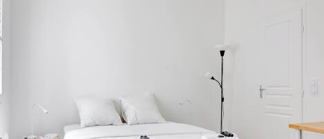 Une chambre d’hôtel minimaliste comprenant un lit, des lampes de chevet, un bureau et une porte.