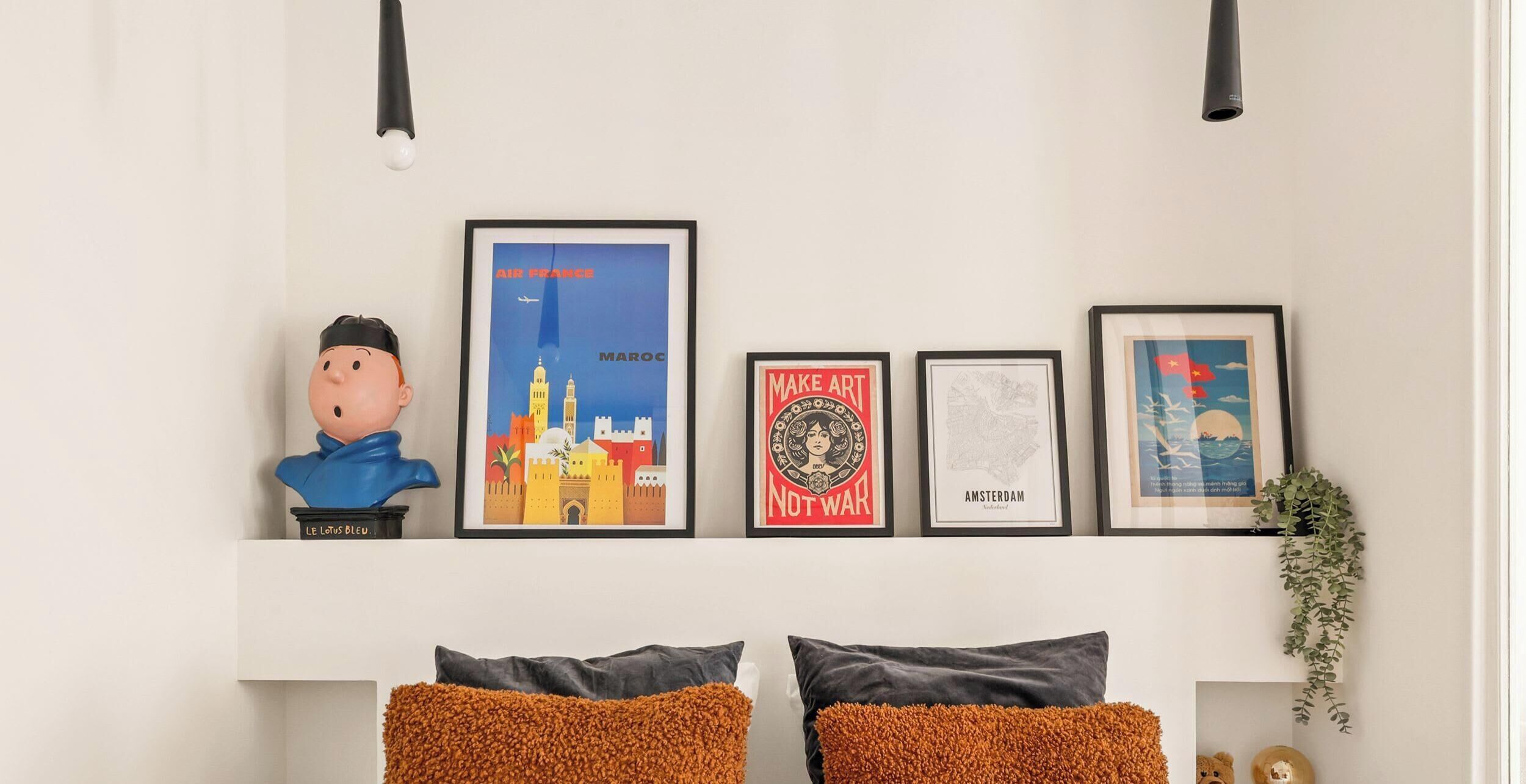 A wall with four framed items, a bust sculpture, and two pillows.
