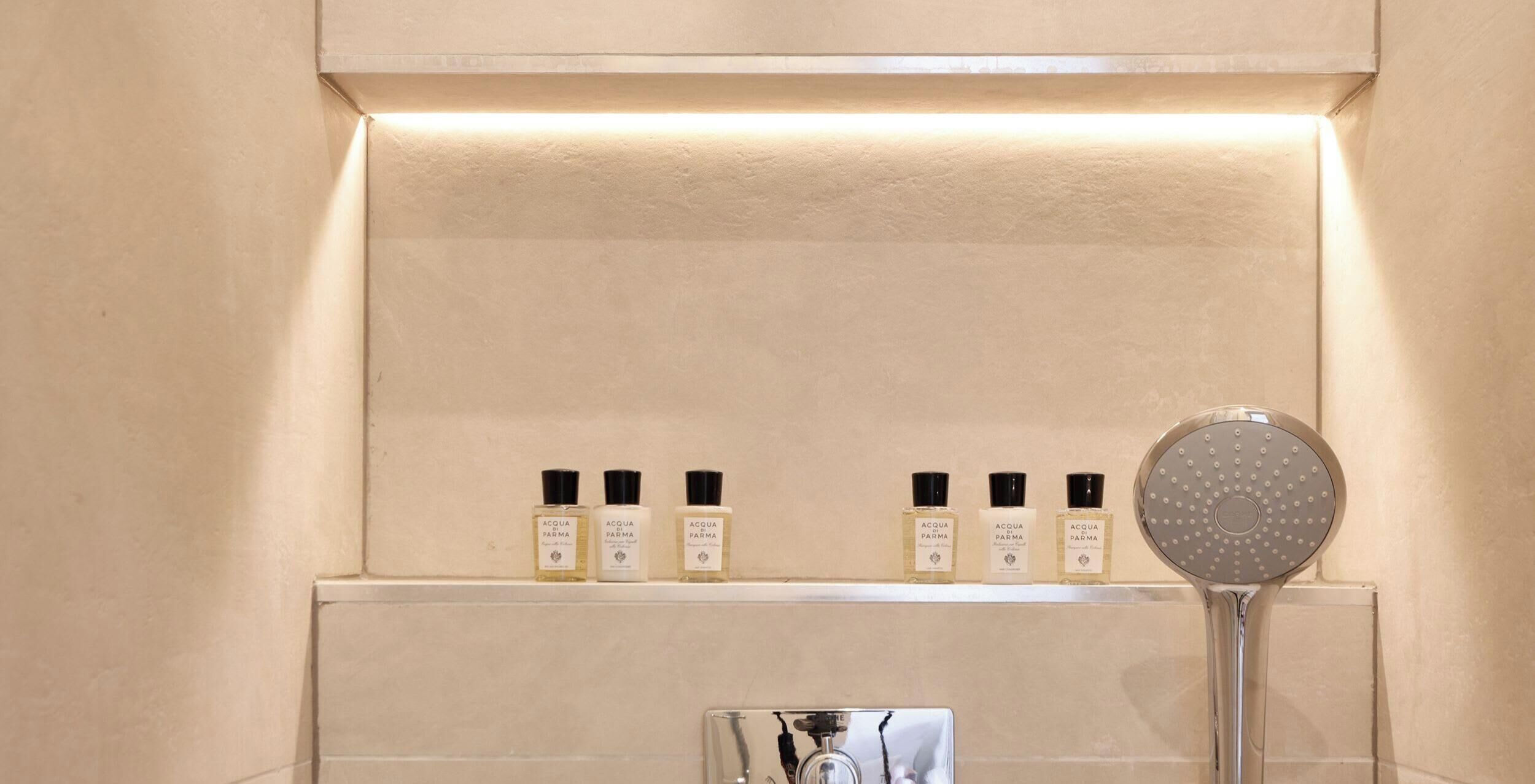 A bathroom with a shelf displaying bottles of Acqua Parma cologne and a handheld showerhead.
