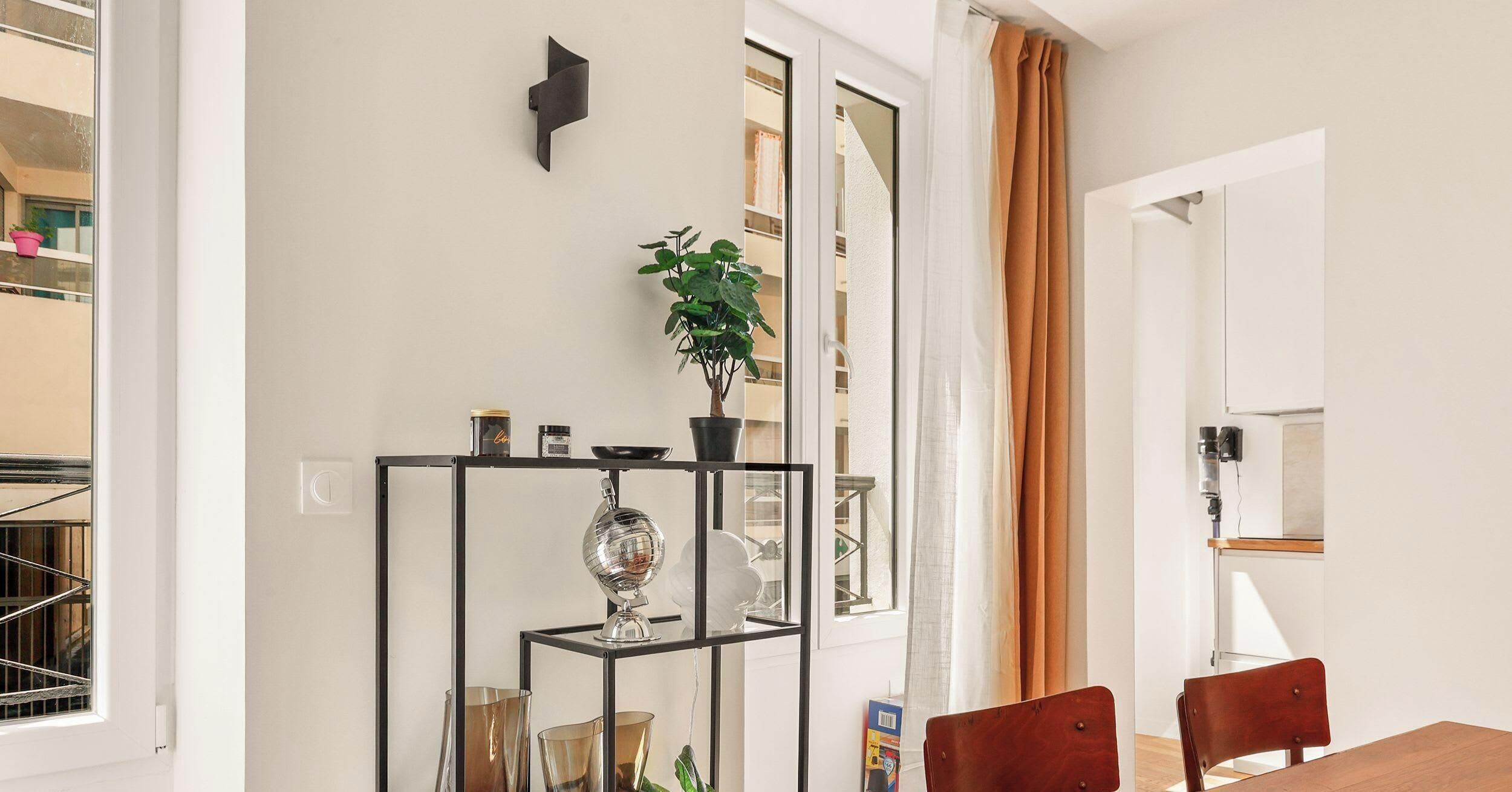 A modern interior with a dining area, a black metal shelf with decorative items, and a potted plant.