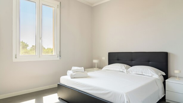 A modern bedroom with a large bed, two bedside tables, and a window.