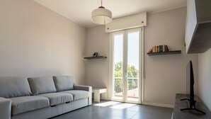 A modern living room with a grey sofa, a flat-screen TV on a stand, and a balcony with a view.