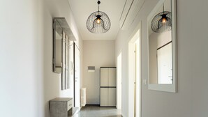 A hallway with a modern design, featuring a central light fixture, a refrigerator, and a mirror on the wall. - Emilia Suite Holiday (Modena)