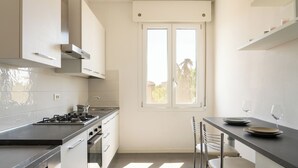 A modern kitchen with a gas stove, stainless steel appliances, a window with a view, and a dining area with chairs and a table. - Emilia Suite Holiday (Modena)