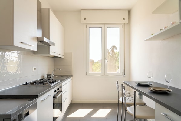 Uma cozinha moderna com fogão a gás, eletrodomésticos de aço inoxidável, uma janela com vista e uma área de refeições com cadeiras e mesa.