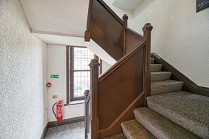 Eine Treppe mit Teppichstufen und einem Holnänder, die zu einer Tür mit Fenster und Notausgangsschild führt.