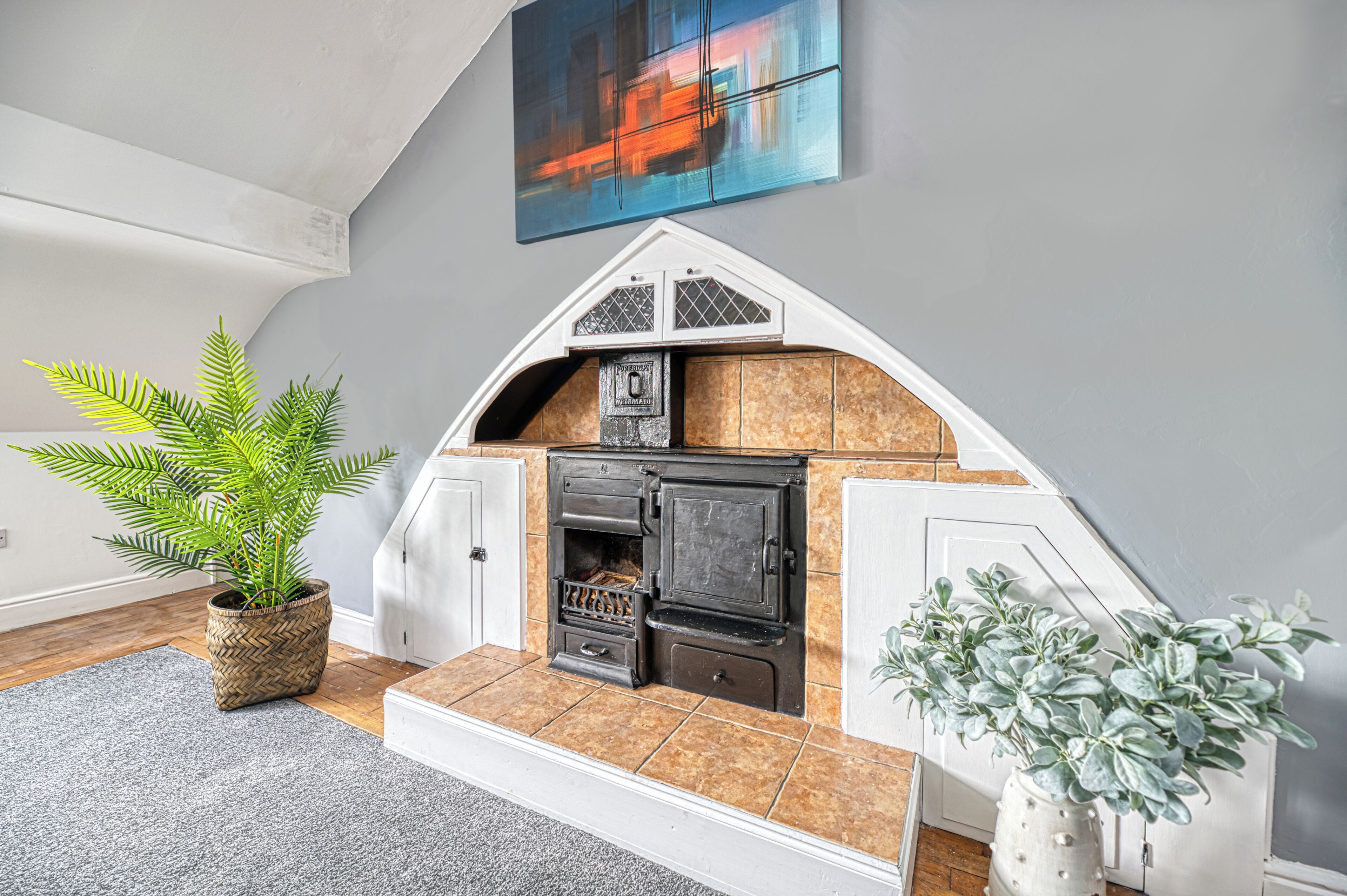 A cozy kitchen with a built-in stove, a potted fern, and a modern painting on the wall.