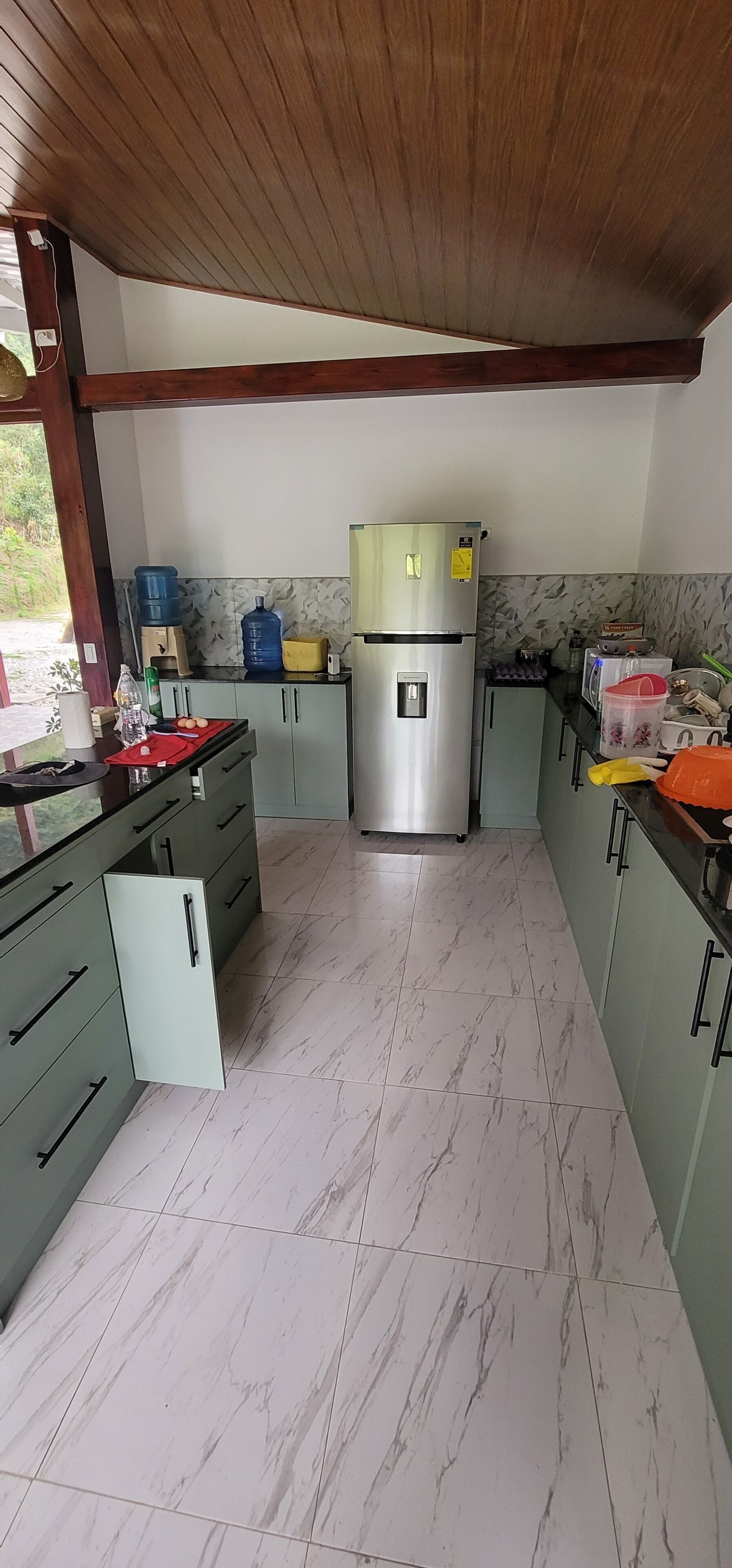 Cozinha com geladeira de aço inoxidável, piso de mármore e armários verdes.