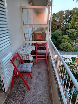 A balcony with a table and two chairs, a window with a view of trees, and a railing. - 2-bedroom apartment in center of Dubrovnik (Dubrovnik)