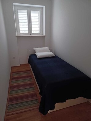 A small, single-bed room with a window above the bed, a striped rug, and a wooden floor. - 2-bedroom apartment in center of Dubrovnik (Dubrovnik)